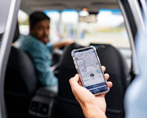 A passenger holds a smartphone displaying a rideshare app while sitting in the back seat of a car, with the driver visible ahead, illustrating rideshare transportation and the legal differences between Uber or Lyft accidents and private car crashes in Colorado Springs.