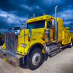 A bright yellow heavy-duty tow truck parked under a dramatic sky, representing commercial trucking operations and the types of large vehicles often involved in serious or fatal semi-truck accidents in Colorado Springs.
