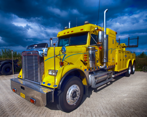 A bright yellow heavy-duty tow truck parked under a dramatic sky, representing commercial trucking operations and the types of large vehicles often involved in serious or fatal semi-truck accidents in Colorado Springs.