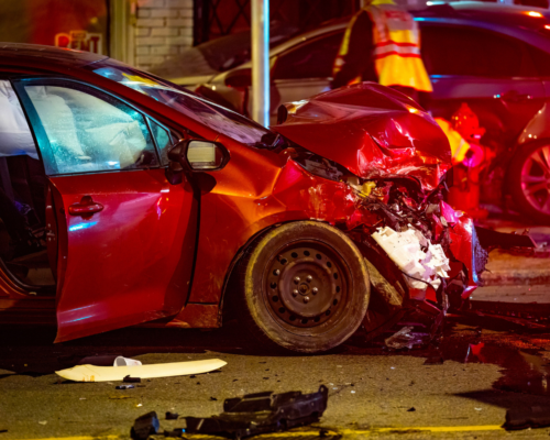 Damaged red car at a crash scene with emergency lights, representing rental car accident injuries, liability, and insurance claims in Colorado Springs.