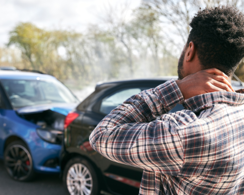 Injured driver holding their neck near damaged vehicles after a crash, representing DUI accident injuries, liability, and compensation claims in Colorado Springs.