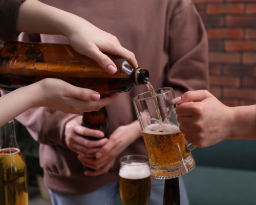 Hands pouring beer into a glass from a bottle while others hold drinks nearby, illustrating alcohol service scenarios relevant to dram shop and social host liability laws in Colorado Springs.