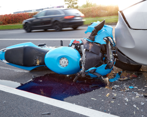 A severely damaged motorcycle lodged against the rear of a car after a crash, highlighting the devastating impact of collisions and the challenges riders face when pursuing insurance claims.