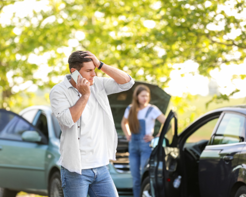 Man on phone at car accident scene with visible vehicle damage, illustrating communication risks with insurance adjusters after a Woodland Park car accident and the importance of legal representation.