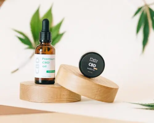 CBD oil bottle on wooden coaster and hanging leaves