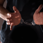A man from the chest down in handcuffs holding his hands in front of him.