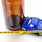 A small plastic toy SUV that has smashed into an empty glass beer bottle with tiny yellow 