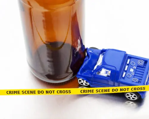 A small plastic toy SUV that has smashed into an empty glass beer bottle with tiny yellow 