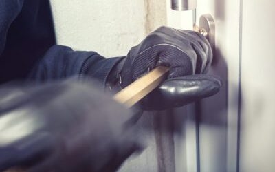 person wearing black leather gloves uses a crowbar to open a locked door.
