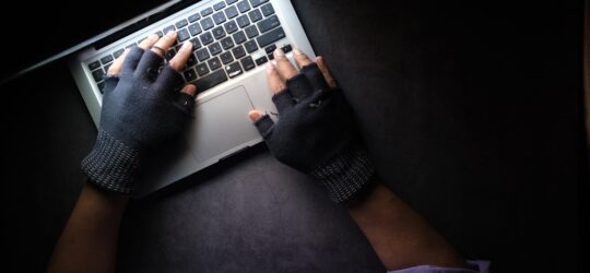 Two gloved hands on a laptop in a dim light room