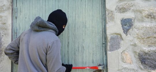 man in a ski mask breaks into a shed with a tool