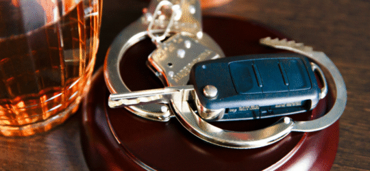 A glass of whiskey next to a car key and handcuffs.