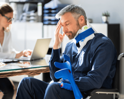 Injured man in neck brace and wheelchair holding crutches, sitting in an office with a concerned expression while meeting with a legal or medical professional, illustrating the aftermath of a personal injury and potential claim consultation