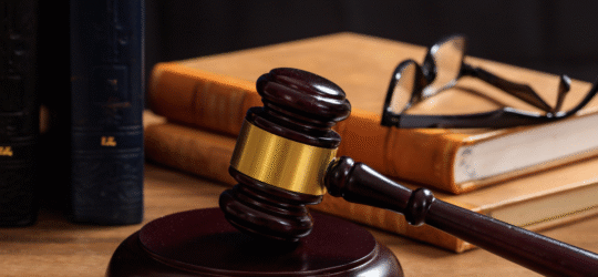 A judges gavel on a table with a lawbook and glasses.