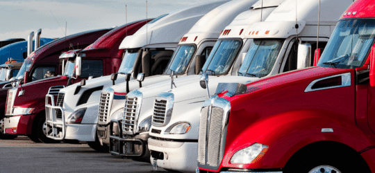Fleet of commercial semi-trucks parked at a trucking company terminal