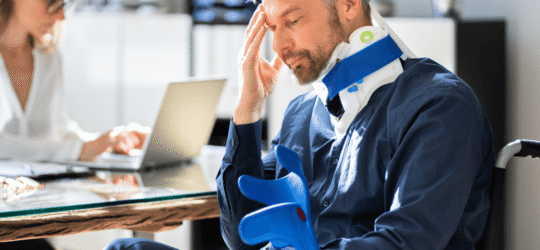 Injured man in neck brace and wheelchair holding crutches, sitting in an office with a concerned expression while meeting with a legal or medical professional, illustrating the aftermath of a personal injury and potential claim consultation