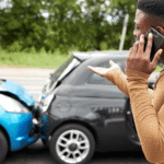 Frustrated driver on phone after rear-end collision between two compact cars, with visible damage to both vehicles, highlighting the aftermath of a traffic accident and the need for legal or insurance assistance